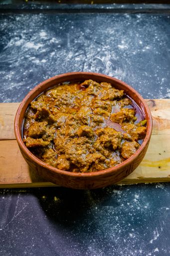 A high-angle shot of a soup with meat in a bowl on the wooden board put on the kitchen table
