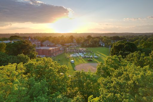An aerial shot of a golden sunrise shining above a small town surrounded by green trees