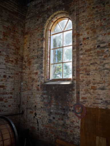 old brick wall with wooden arched window with small planes of grass.  Background in colour.