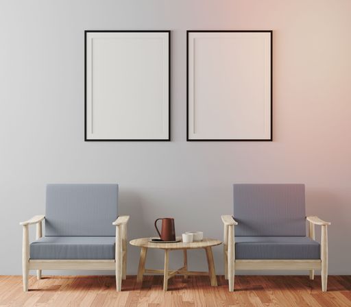 An interior shot of two blank frames hanging on a wall with gray armchairs under it, with copy space