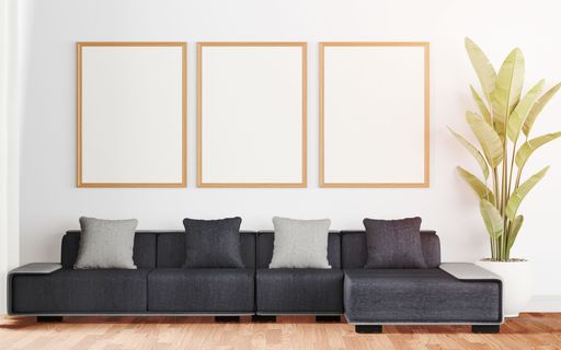 An interior room featuring three white frames hanging above a gray couch, with copy space