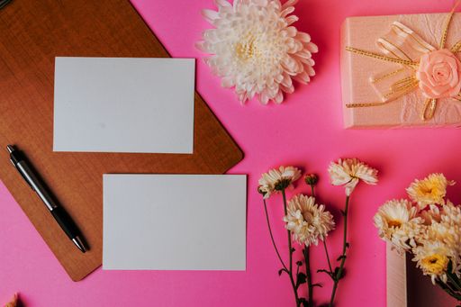 A pink surface with fresh flowers, two blank cards, and a pen, with copy space