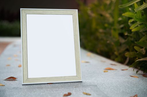 A white picture frame set against a green foliage background, with copy space