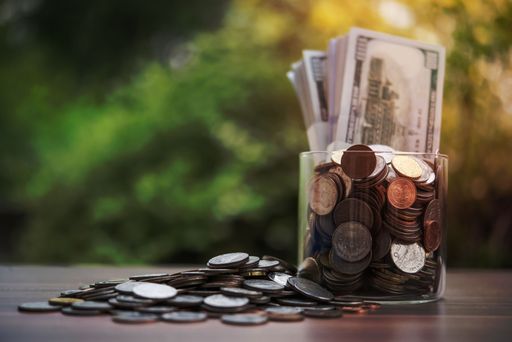A closeup of a pile of coins and euro banknotes in a glass jar on a wooden table