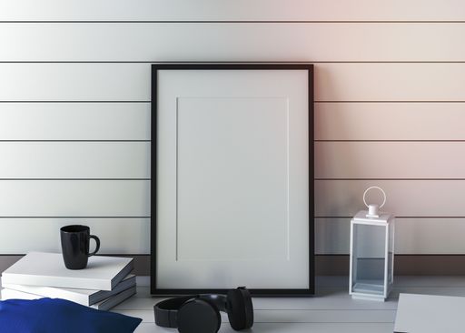 A blank white picture frame, books, headphones, and a tea cup on a table in the office
