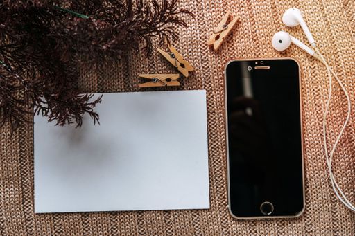 A top view of a blank postcard, earphones, clothpins, and a smartphone