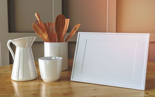A white blank picture frame and kitchen utensils in a jar on a wooden table