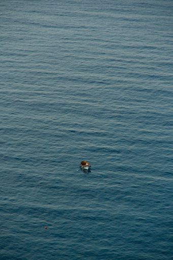 An aerial shot of a small wooden boat in the middle of the Mediterranean sea turquoise