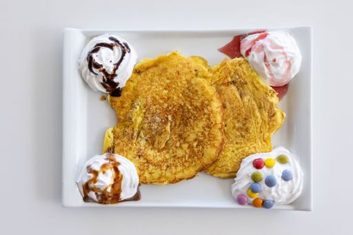 A top view of a pancake serving with whip cream and sweets placed on a white table