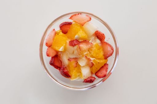 A top view closeup of a fruit bowl with fresh strawberries and orange slices on a white surface