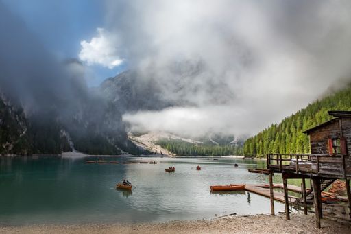 A beautiful scenery of people with small boats in a lake surrounded by trees and mountains under sky full of clouds