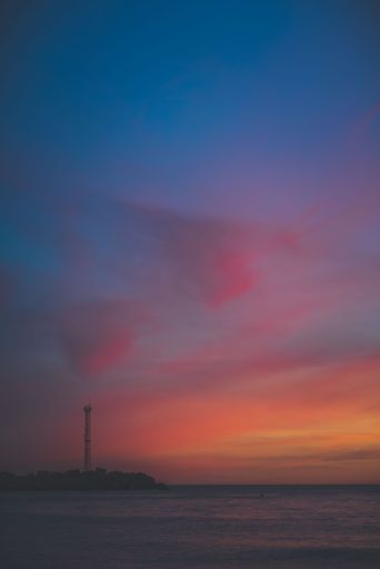 A vertical shot of a beautiful sunset over a tranquil sea against a lighthouse on the beach