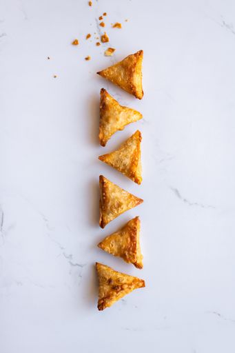 Fried samosa (samoosas) triangle pastries on a white marble surface. Photographed from a