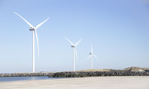 A line of white windmills near the sea under the beautiful blue sky