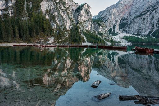A range of boats in the Braies Lake with the reflection of high rocky mountains in Italy