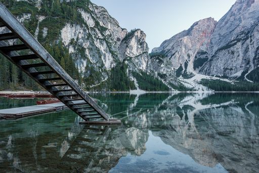 A beautiful scenery of high rocky mountains reflected in Braies lake with wooden stairs near the pier in Italy