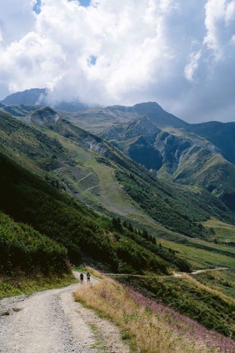 A vertical shot of people hiking through a path surrounded with beautiful mountains under a cloudy sky