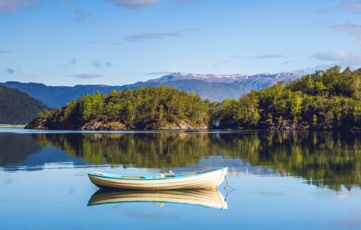 A small wooden white boat floating on the surface of a lake surrounded by trees and vegetation