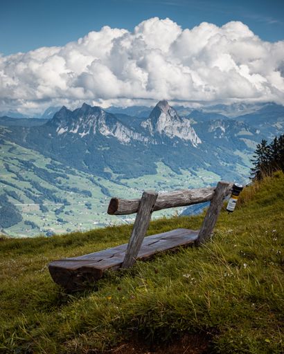 A vertical view of a wooden bench on a slope facing the scenic view of the mountains