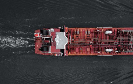 An aerial view over a red cargo ship under the sunlight in a sea