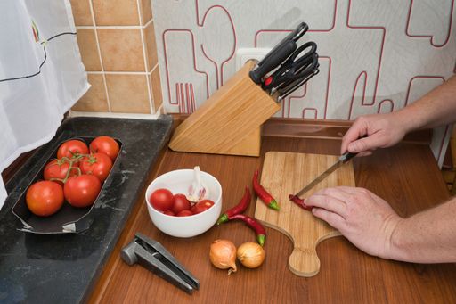 male hands, man, cutting red chillies and preparing a salsa with onions, garlic and tomatoes in kitchen