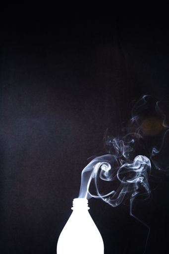 The smoke coming out of a plastic bottle on black background -  aromatherapy concept