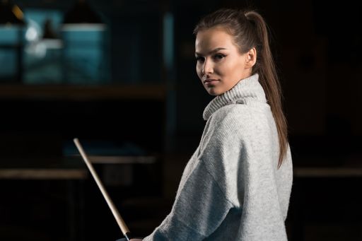 A closeup of a beautiful young woman with a cue stick looking at the camera.