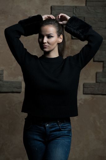 A vertical shot of a young female doing her hair while standing before a brown wall