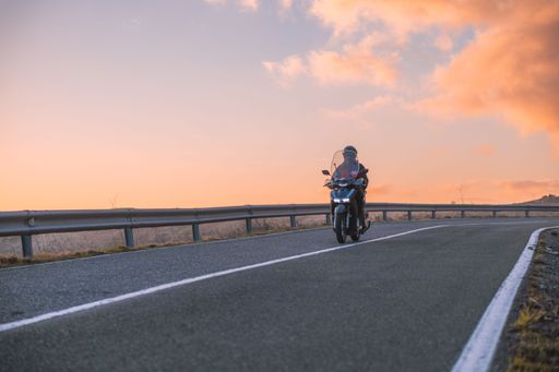 A male riding motorcycle on road during sunset