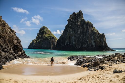The woman standing on the beach and looking at cliffs. Cacimba do Padre, Fernando de Noronha, Brazil.
