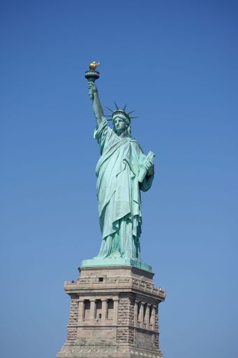 A vertical shot of the Statue of Liberty under a blue sky
