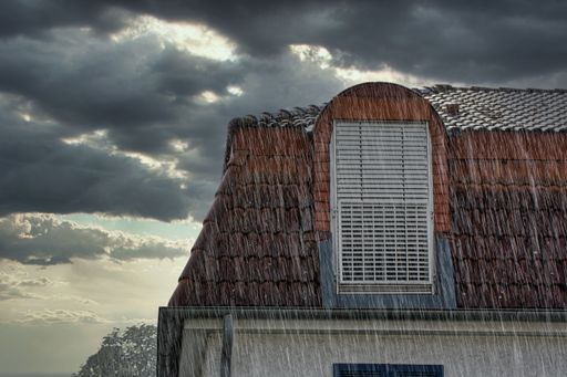 Roof and window of a modern house in a heavy rain shower with dark sky in background