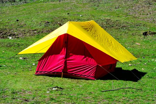 Red and yellow camping tent in the middle of a green grass field forest