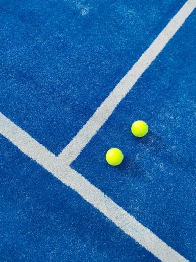 A vertical top view of two green balls on a blue artificial grass paddle tennis court by white line