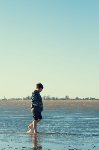 A vertical shot of a Caucasian boy walking along the seashore at daytime