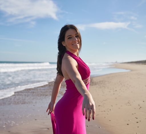 A vertical shot of a beautiful young woman posing on the beach wearing a dress