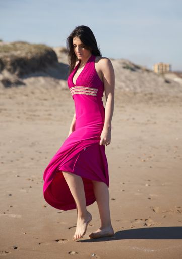 A vertical shot of a beautiful young woman posing on the beach wearing a dress