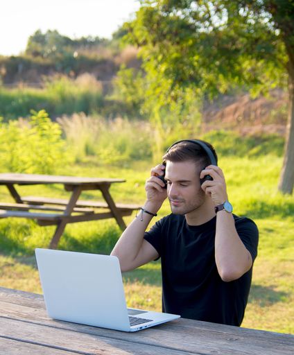 A young caucasian male with headphone working with his laptop in the nature