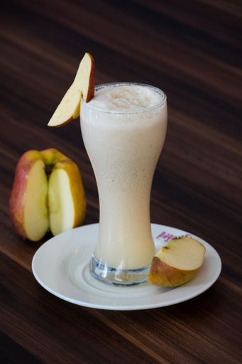 A vertical shot of apple smoothie in an elongated glass cup on a wooden table background