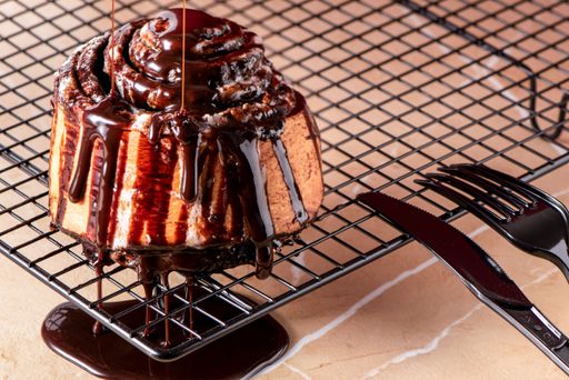 A closeup shot of a delicious cinnamon roll on the oven net tray with drizzles of melted chocolate