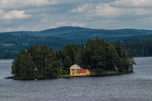 A beautiful view of a small island on a lake surrounded by vast hills covered by dark trees on a cloudy day