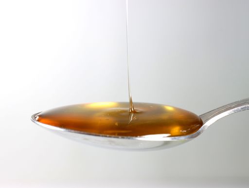 A closeup shot of a silver spoon filled with honey on a white background