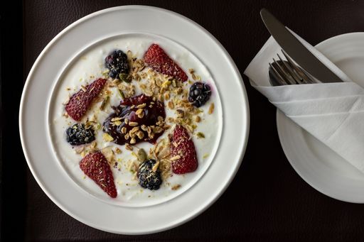 A top view of yogurt garnished with berries, strawberry and nuts with neatly wrapped cutlery next to it