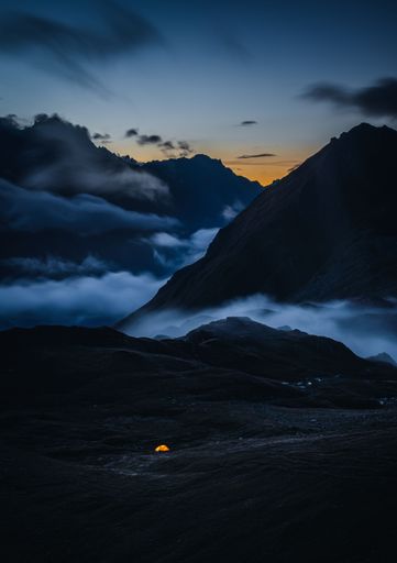 A beautiful view of a tent in the middle of a hill surrounded by mountains
