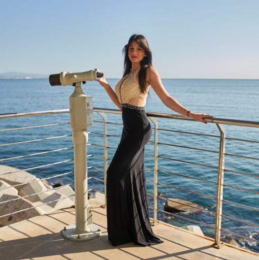 A vertical shot of a sexy young woman posing in the beach near a binocular