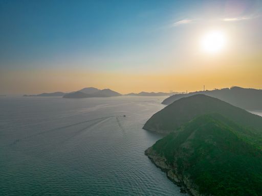 An aerial view of sea with boats surrounded by greenery mountains during sunrise