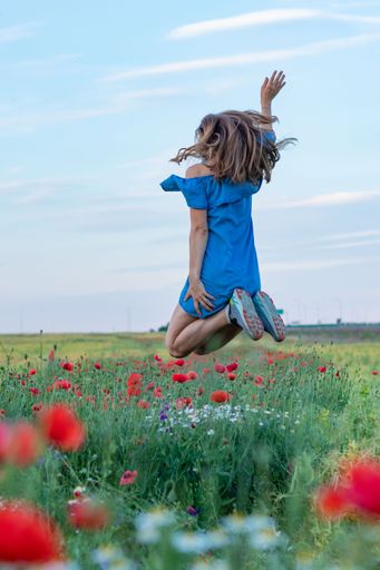 A vertical shot of a girl jumping in the green poppy field
