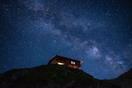 A wooden house on the edge on the edge f a hill with a bright starry night sky in the background