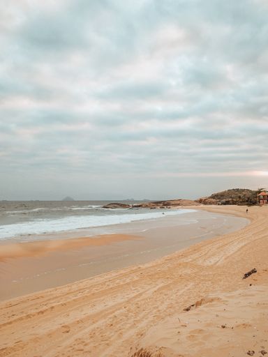 A vertical shot of a beach surrounded by the sea under a cloudy sky in Rio de Janeiro, Brazil