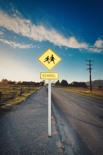 A vertical shot of a yellow signpost about children crossing the road near the school